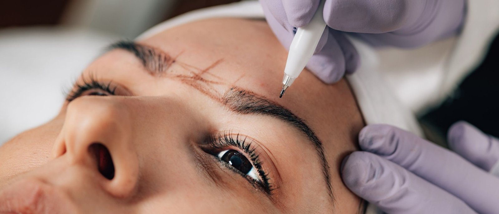 A brow artist applying pigment in fine hair-strokes over a mapped brow at Plum & Sugar